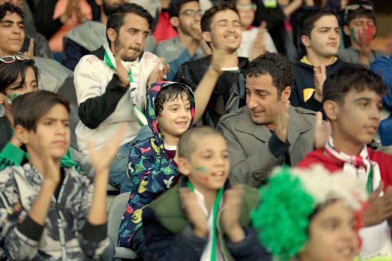 Zróżnicowany tłum podekscytowanych fanów, w tym dzieci i dorośli, klaszcze i uśmiecha się, oglądając wydarzenie. Niektórzy mają pomalowane twarze, a jedno dziecko w kolorowej bluzie z kapturem siedzi obok mężczyzny, który patrzy na nie ciepło.