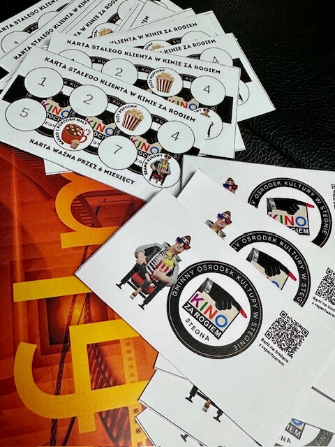 Kilka kart lojalnościowych do kina o nazwie Kino za Rogiem rozłożonych na powierzchni. Karty mają kółka na znaczki, grafiki popcornu i loga. Tekst na kartach jest po polsku.
