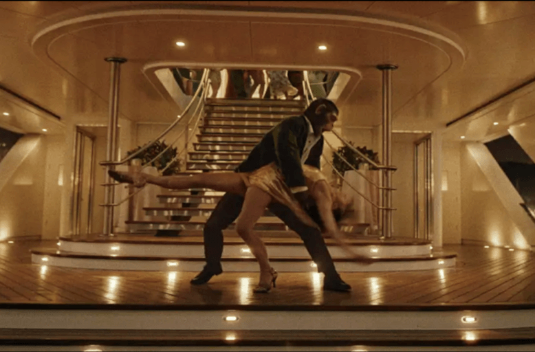 Mężczyzna w garniturze i kobieta w żółtej sukience wykonują dramatyczną pozę taneczną na pokładzie luksusowego jachtu, z szerokimi schodami i eleganckim oświetleniem w tle.