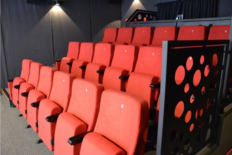 Rzędy pustych, jaskrawoczerwonych foteli kinowych z czarnymi podłokietnikami są ustawione w rzędach. Każde siedzenie jest oznaczone numerem, a obszar jest oświetlony kinkietami, co nadaje nowoczesny wygląd teatru.