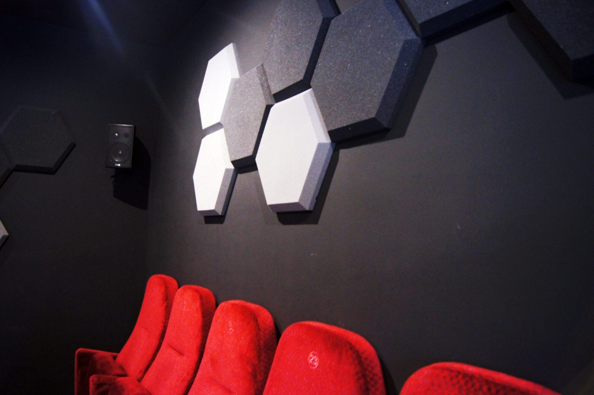 Cztery czerwone fotele teatralne ustawione są wzdłuż czarnej ściany. Ściana jest ozdobiona dużymi czarno-białymi sześciokątnymi panelami akustycznymi, a głośnik jest zamontowany w lewym górnym rogu.