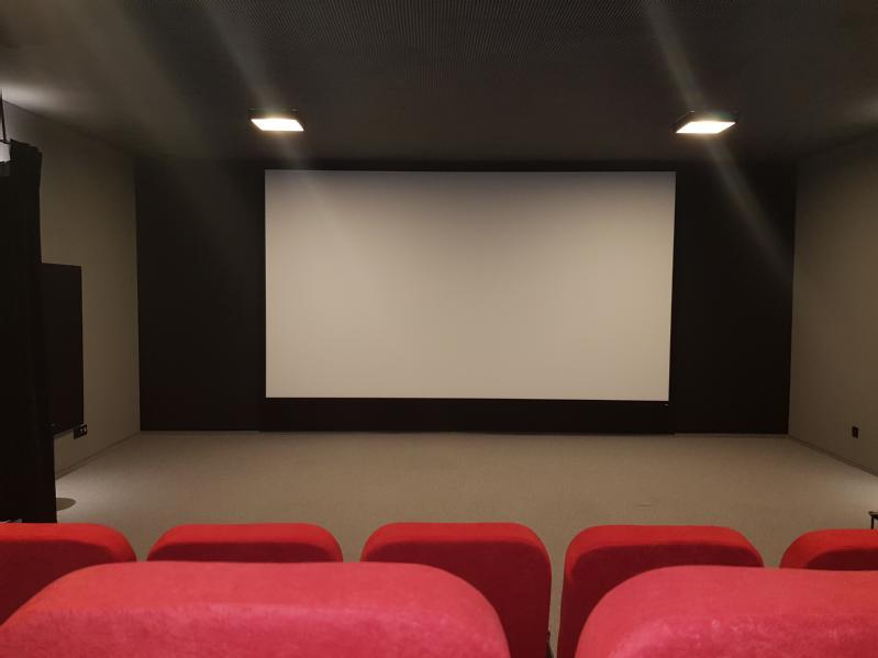 Małe, puste kino z czerwonymi siedzeniami i dużym, pustym ekranem z przodu, oświetlonym lampami sufitowymi.