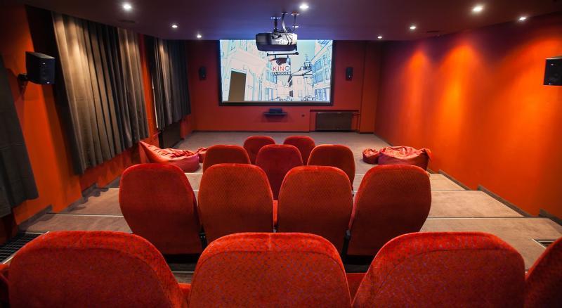 Małe kino z czerwonymi, wyściełanymi siedzeniami, czerwonymi ścianami, workami sako z przodu i filmem wyświetlanym na dużym ekranie. W pomieszczeniu jest słabe oświetlenie i zasłony wzdłuż ścian.
