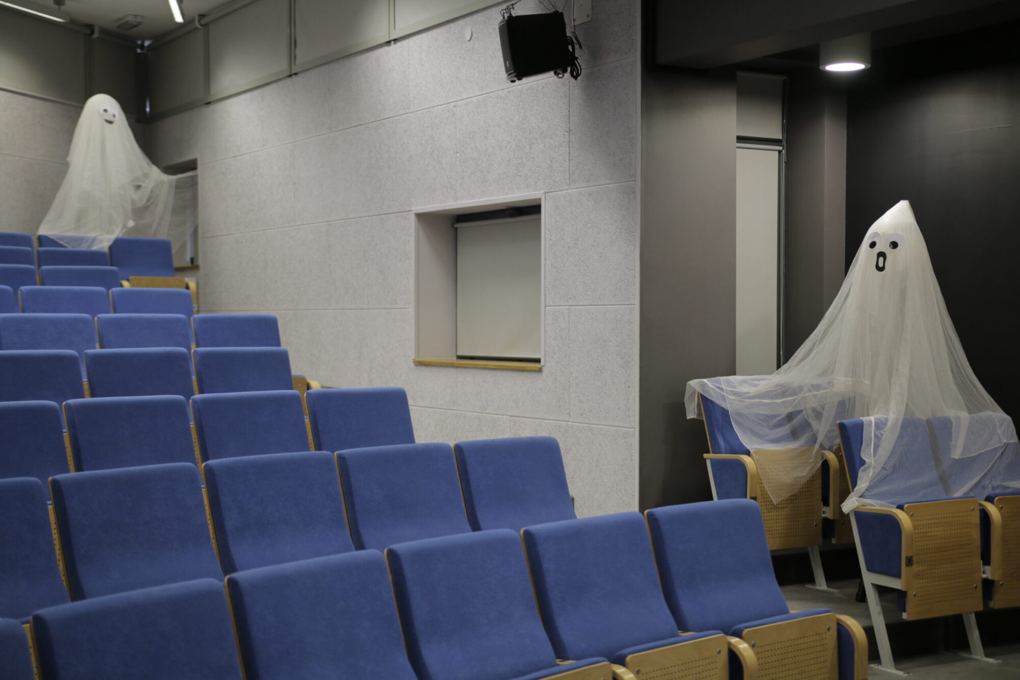 Prawie pusta widownia z niebieskimi siedzeniami ozdobiona jest dwoma dekoracjami przedstawiającymi duchy wykonanymi z białych prześcieradeł z narysowanymi twarzami. Jedna z nich siedzi na siedzeniu, a druga wisi na ścianie w rogu.