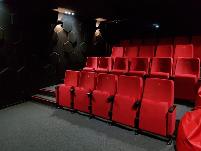 Puste kino z trzema rzędami jaskrawoczerwonych siedzeń, podłokietnikami i ciemnymi ścianami o heksagonalnym wzorze. Oświetlenie jest przyćmione, co tworzy przytulną i cichą atmosferę.