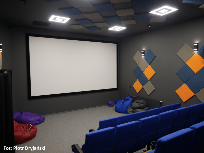 Małe nowoczesne kino domowe z niebieskimi siedzeniami, dużym pustym ekranem, kolorowymi panelami akustycznymi na ścianach i workami sako na podłodze. Autor zdjęcia: Piotr Dryjański.