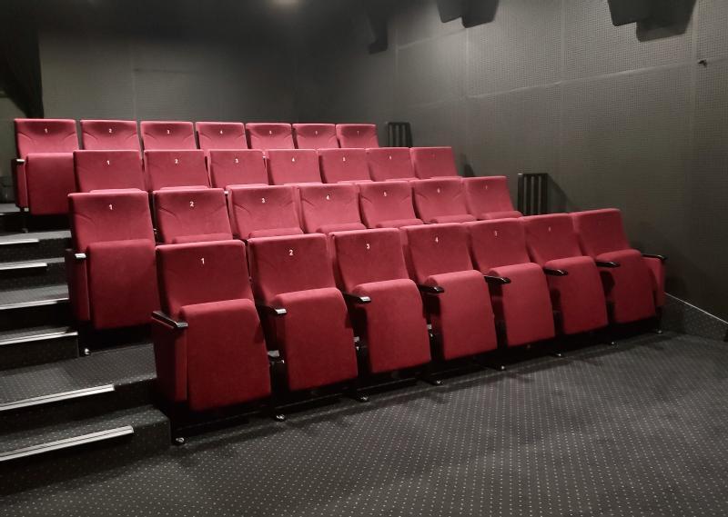 Małe, puste kino z trzema rzędami czerwonych, wyściełanych siedzeń na dywanowej podłodze. Ściany są ciemne i proste, a nie ma tam żadnych ludzi.
