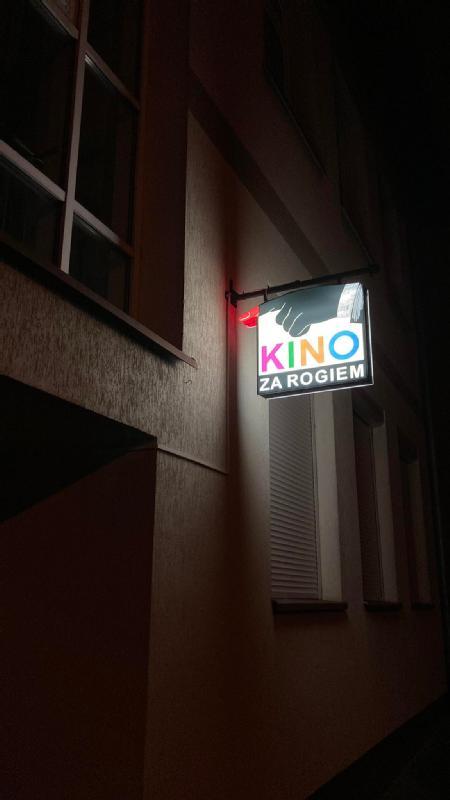 Świecący napis Kino za Rogiem z kolorowymi literami widnieje na zewnętrznej ścianie budynku.