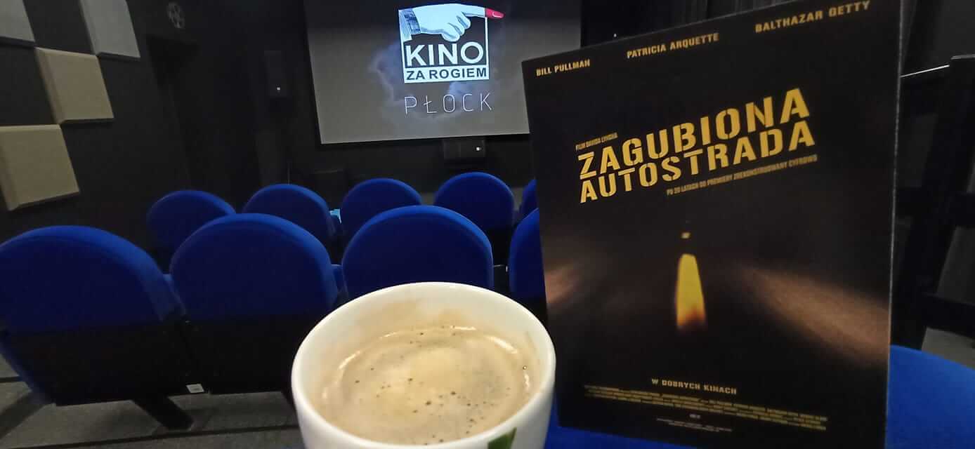 Filiżanka kawy, bilet do kina Zagubiona Autostrada i niebieskie fotele kinowe przed ekranem wyświetlającym Kino za Rogiem Płock w małym kinie.