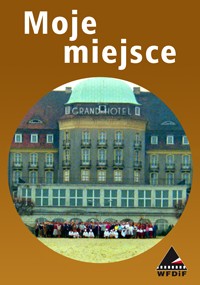 Zdjęcie na okładce z polskim tytułem Moje miejsce nad fotografią grupy ludzi stojących przed dużym budynkiem z napisem Grand Hotel, na brązowym tle i z logo WFDIF w prawym dolnym rogu.