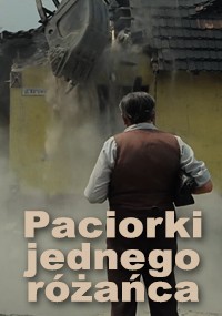Mężczyzna o siwych włosach stoi tyłem do kamery, patrząc na rozpadający się, zakurzony budynek; z dachu spadają gruzy. Na dole nałożony jest polski tekst Paciorki jednego różańca.