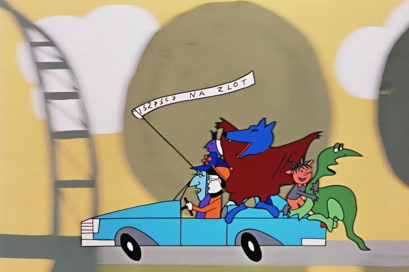 Ludzie z kreskówek i kolorowe fantastyczne stworzenia jadą niebieskim kabrioletem. Nad samochodem widnieje baner WSZYSCY NA ZLOT. Tło jest abstrakcyjne z dużymi drzewami i strukturą kolejki górskiej.