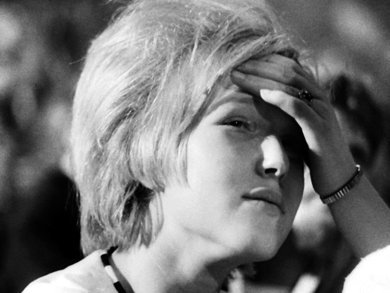 Czarno-białe zdjęcie młodej osoby z krótkimi, jasnymi włosami, opierającej rękę na czole i patrzącej lekko w górę z zamyślonym lub zaniepokojonym wyrazem twarzy.