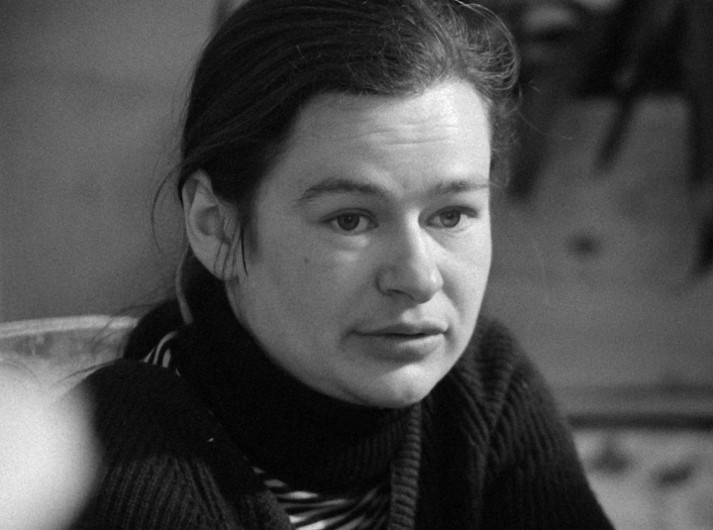 Czarno-białe zdjęcie kobiety o ciemnych włosach, ubranej w pasiasty golf, wyglądającej nieco poza kadrem, z zamyślonym wyrazem twarzy.