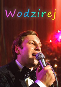 Mężczyzna w garniturze i muszce w kropki trzyma mikrofon i mówi lub śpiewa. Nad nim na ciepłym, świątecznym tle pojawiają się kolorowe litery tworzące słowo Wodzirej.