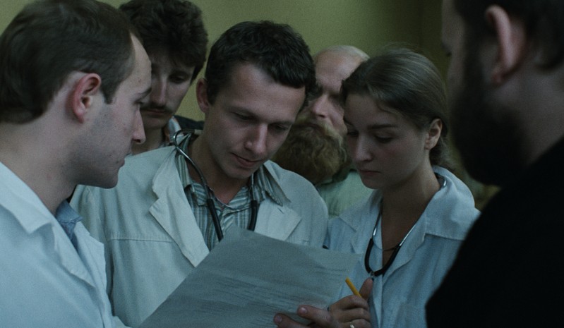 Grupa lekarzy ubranych w białe fartuchy i stetoskopy wspólnie w warunkach klinicznych szczegółowo bada dokument.