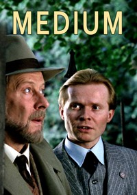 Dwóch mężczyzn w strojach z początku XX wieku stoi na zewnątrz, jeden w kapeluszu, a drugi w garniturze w paski, patrząc uważnie w bok. Na górze widnieje napis MEDIUM dużymi żółtymi literami.