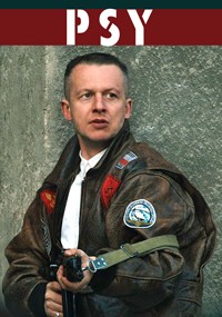Mężczyzna w brązowej skórzanej kurtce trzyma pistolet i patrzy w bok. Stoi przy teksturowanej szarej ścianie, nad nim na czerwonym banerze widnieje napis PSY w pogrubionych białych literach.