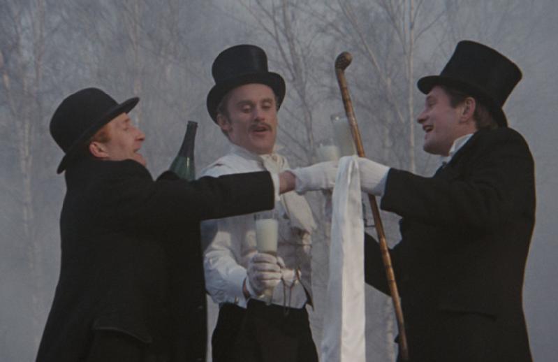 Trzech mężczyzn w smokingach i cylindrach wznosi toast szklankami mleka na zewnątrz, wśród drzew i mgły. Jeden z nich trzyma laskę, a oni wydają się świętować, uśmiechać się i być radośni.