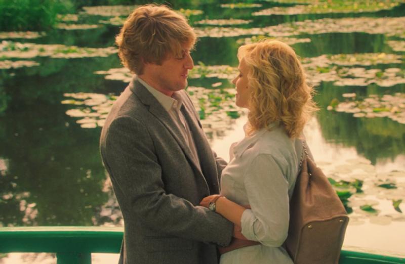 Mężczyzna i kobieta stoją blisko siebie na zielonym moście nad stawem z liśćmi grzybieni, patrząc na siebie z uczuciem. Tło jest bujne i zielone, tworząc romantyczną atmosferę.