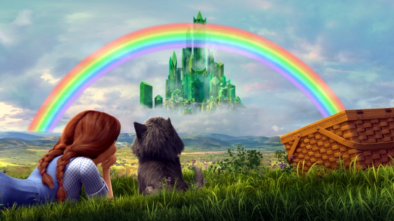 Dziewczynka z warkoczami i mały pies leżą na trawie, patrząc na zielony kryształowy zamek w oddali, z jasną tęczą wyginającą się na błękitnym niebie. W pobliżu stoi kosz piknikowy.