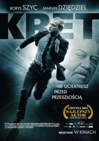Plakat filmowy Kreta przedstawiający mężczyznę w garniturze biegnącego z poważnym wyrazem twarzy. W tle widoczna jest duża twarz, a także polski tekst wraz z napisami końcowymi i nagrodą.