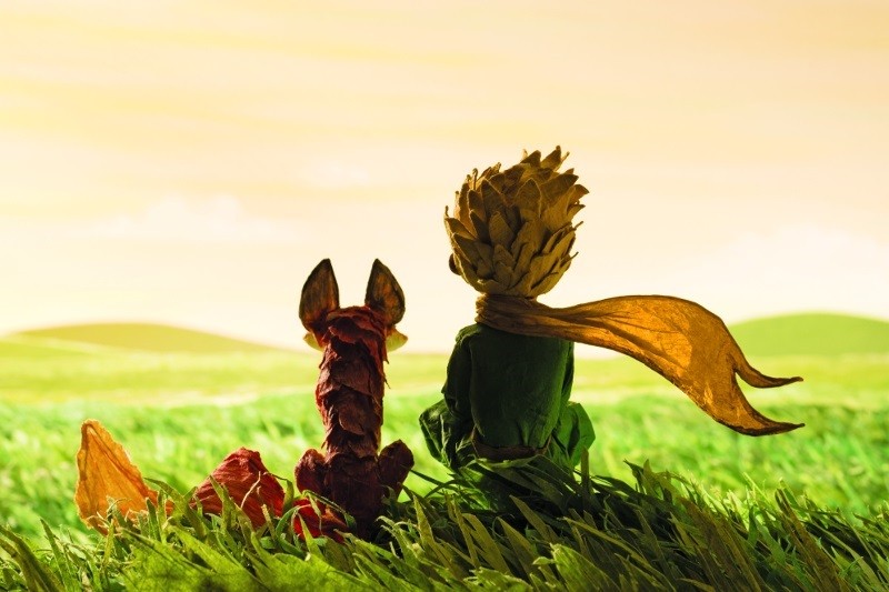 Mała postać ubrana w żółty szalik siedzi obok lisa na trawiastym wzgórzu. Oboje patrzą na złote niebo i odległe pagórki, co przywodzi na myśl spokojną, kontemplacyjną scenę.