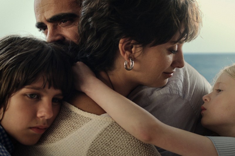 Czteroosobowa rodzina trzyma się blisko siebie, jej twarze są pełne poważnych i emocjonalnych emocji, a tło jest rozmazane.