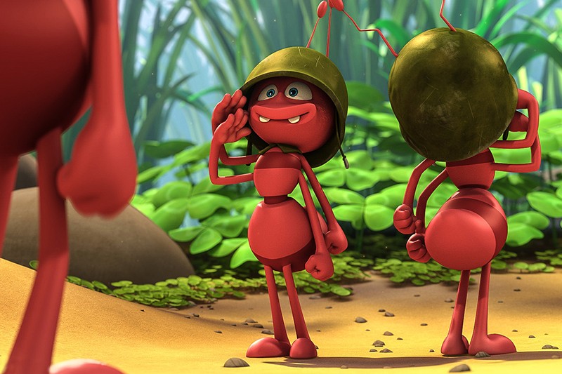 Dwie animowane czerwone mrówki, noszące zielone hełmy, stoją na piaszczystym podłożu otoczonym roślinami. Jedna mrówka salutuje z uśmiechem, podczas gdy druga stoi odwrócona plecami. Inna mrówka jest częściowo widoczna po lewej stronie.