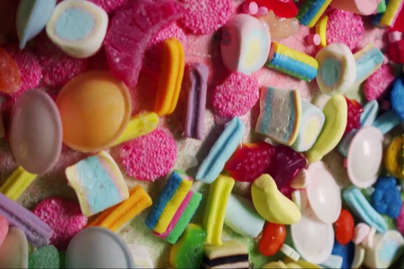 Kolorowy asortyment różnych cukierków, w tym żelek, lukrecji, pianek i galaretek, rozrzuconych blisko siebie na jasnej powierzchni.