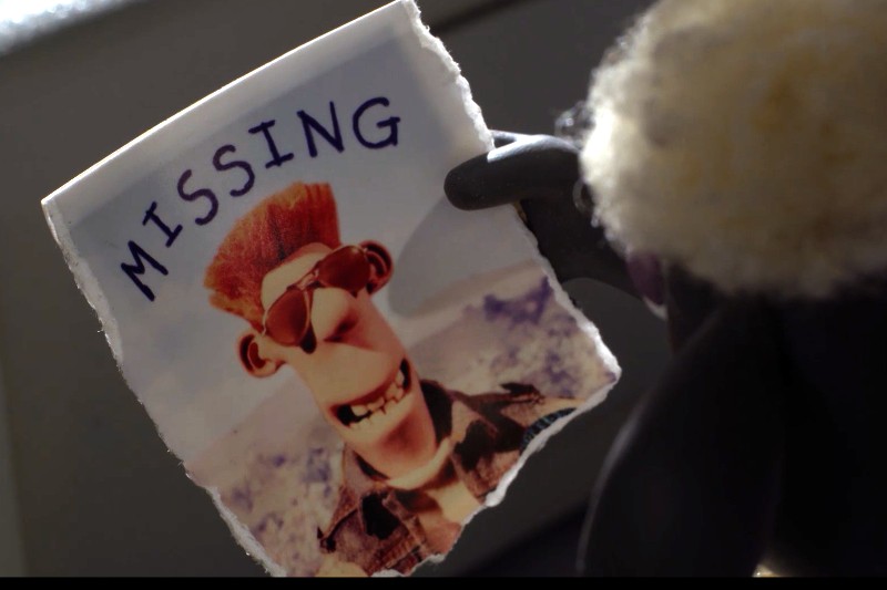 Ręka w rękawiczce trzyma podarty plakat z informacją o zaginięciu, na którym widnieje postać z kreskówki o sterczących włosach, w okularach przeciwsłonecznych i z szerokim uśmiechem, na rozmytym tle otoczenia.