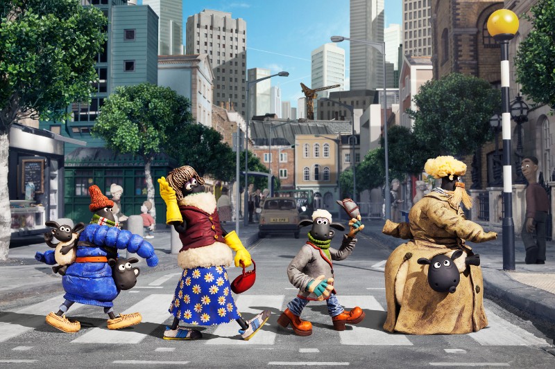 Cztery owce z animacji poklatkowej, ubrane w kolorowe zimowe ubrania, przechodzą przez miejskie przejście dla pieszych, naśladując słynne zdjęcie Beatlesów z Abbey Road. W tle widać wysokie budynki i drzewa.