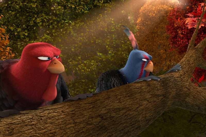 Dwa animowane indyki, jeden czerwony i jeden niebieski, kucają za opadłą gałęzią drzewa w lesie z kolorowymi jesiennymi liśćmi, oba wyglądają na czujne i skupione. Światło słoneczne przesącza się przez drzewa nad nimi.