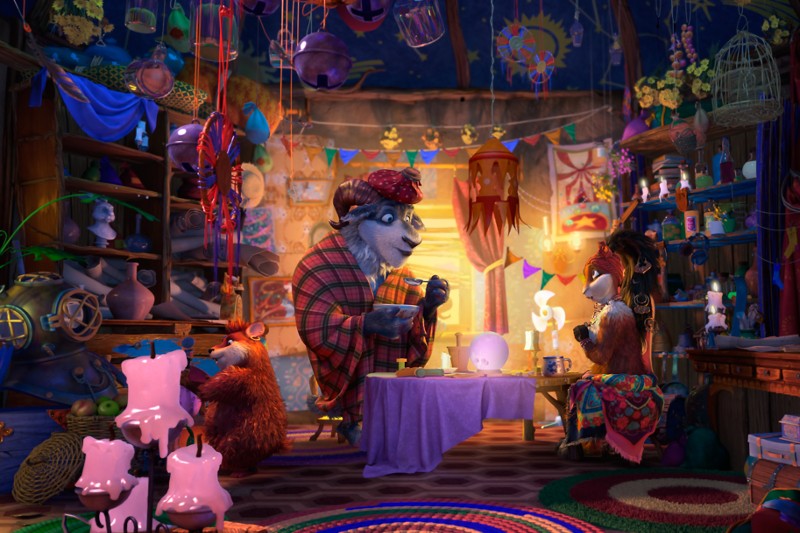Trzy kolorowe postacie zwierząt, ubrane w jaskrawe ubrania, siedzą przy stole w przytulnym, zagraconym i fantazyjnie udekorowanym pokoju wypełnionym artykułami artystycznymi, świecami, wiszącymi ozdobami i ciepłym, migoczącym światłem.