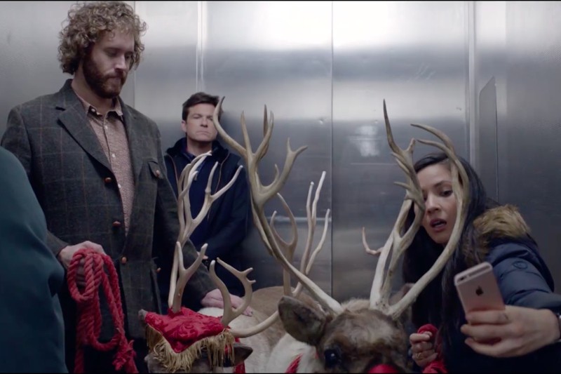 Trzy osoby i dwa renifery stoją w windzie. Kobieta po prawej robi sobie selfie telefonem, trzymając poroże renifera. Obok niej stoją dwaj mężczyźni, jeden trzyma lejce, a drugi patrzy w górę.