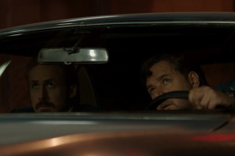 Dwóch mężczyzn siedzi w samochodzie nocą; jeden prowadzi i patrzy w górę przez przednią szybę, podczas gdy drugi siedzi na siedzeniu pasażera z poważnym wyrazem twarzy. Wnętrze jest słabo oświetlone.