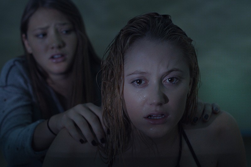 Dwie młode kobiety są w słabo oświetlonej scenie. Kobieta z przodu wygląda na mokrą, zdenerwowaną i przestraszoną, podczas gdy kobieta za nią delikatnie kładzie ręce na jej ramionach, wyglądając na zaniepokojoną.