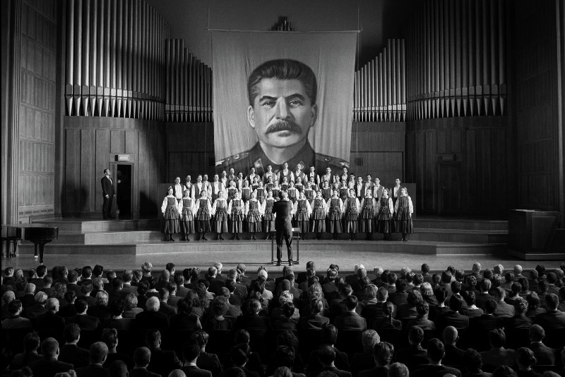 Chór występuje na scenie przed publicznością, a za nimi wisi duży portret Józefa Stalina. Sceneria wydaje się być salą koncertową z piszczałkami organowymi i drewnianymi panelami.