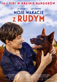 Chłopiec ubrany w kraciastą koszulę uśmiecha się i przytula brązowego psa. W tle widać naturalne otoczenie na zewnątrz z niebieskim niebem. Nad nimi znajduje się tytuł polskiego filmu Moje Wakacje z Rudym.