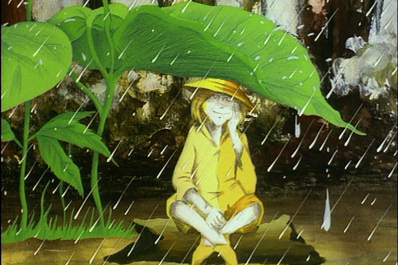 Osoba w żółtym płaszczu przeciwdeszczowym i kapeluszu siedzi na skale, chroniąc się pod dużym, zielonym liściem podczas burzy, podczas gdy wokół niej pada ulewny deszcz.