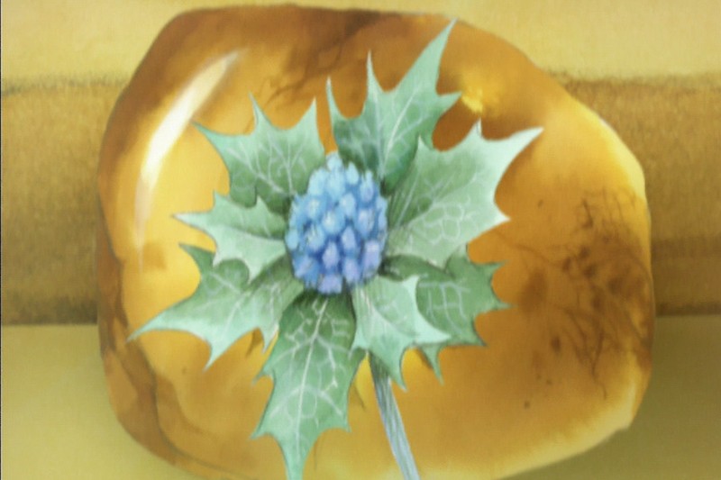 Pojedynczy niebieski kwiat ostu z kolczastymi zielonymi liśćmi umieszczono przed dużym, gładkim, bursztynowym kamieniem na żółtej powierzchni.