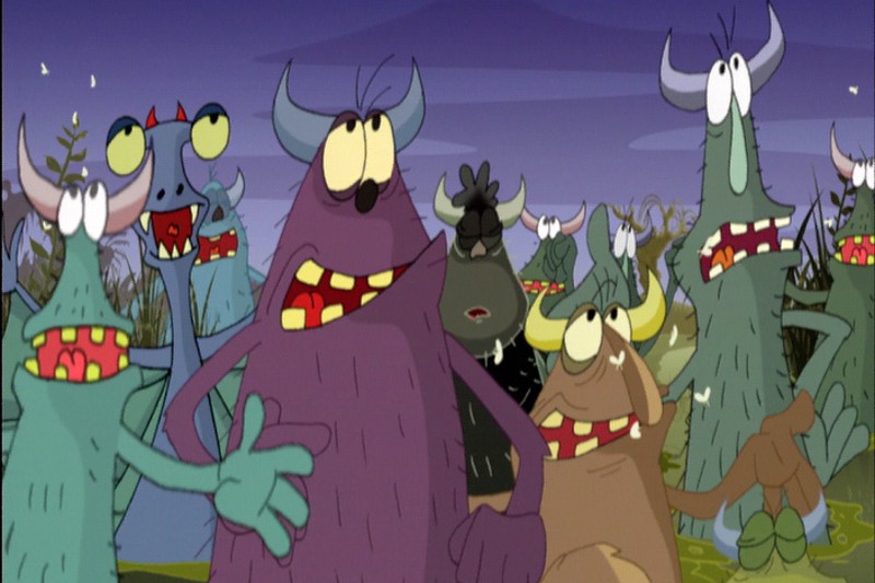 Kreskówkowe, kolorowe potwory z rogami i dużymi zębami stoją razem na zewnątrz o zmierzchu, wyglądając na zaskoczonych lub zdezorientowanych. Tło przedstawia trawę i fioletowe niebo. Potwory są futrzaste i występują w różnych kształtach i kolorach.