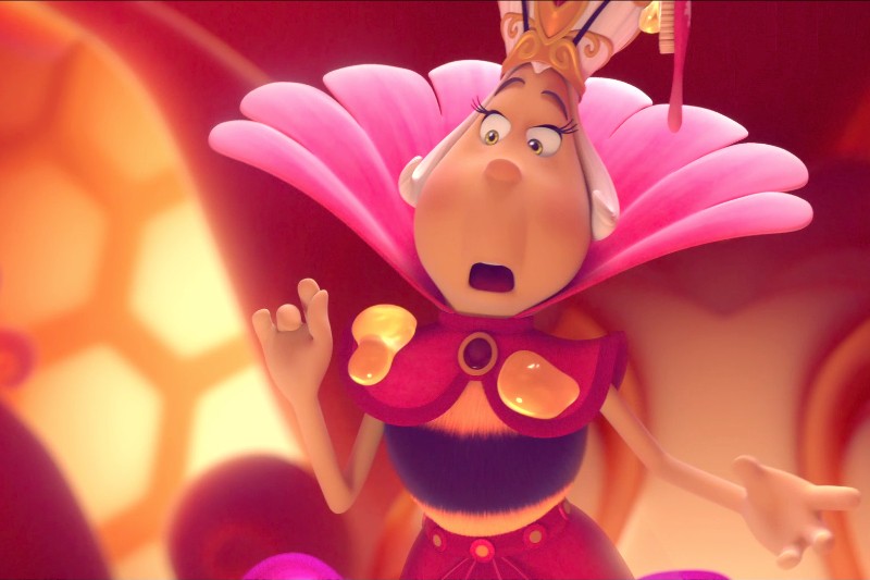 Animowana królowa pszczół w koronie i z dużym, różowym kołnierzem przypominającym płatki kwiatów, wygląda na zaskoczoną, z otwartą buzią i uniesioną ręką, a wszystko to w jaskrawo kolorowym, świecącym otoczeniu.