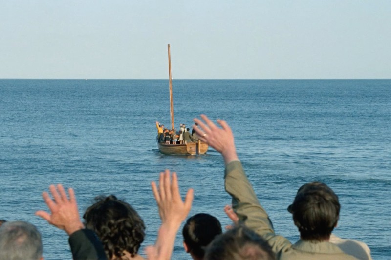 Ludzie stoją na brzegu i machają na pożegnanie małej drewnianej łódce, która przewozi pasażerów na morze pod czystym niebem.