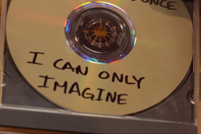 Zbliżenie na złotą płytę CD w przezroczystym pudełku z napisem I CAN ONLY IMAGINE napisanym odręcznie czarnym markerem.