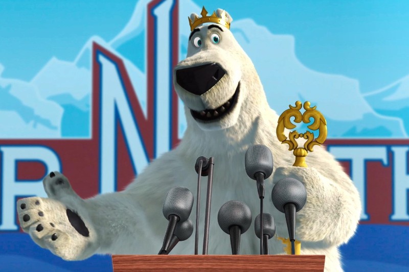 Kreskówkowy niedźwiedź polarny w złotej koronie i trzymający ozdobną laskę stoi za podium z kilkoma mikrofonami, wydając się wygłaszać przemowę na tle lodowego motywu.