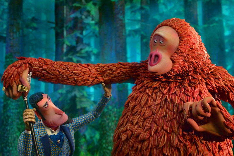 Dobrze ubrany, animowany mężczyzna trzyma za rękę dużego, rudowłosego Sasquatcha w bujnym, zielonym lesie. Sasquatch wygląda na zaskoczonego, gdy mężczyzna patrzy na niego.