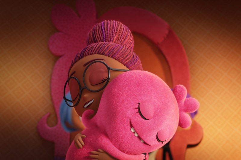 Uśmiechnięta animowana dziewczynka w okularach i fioletowych włosach przytula puszyste różowe stworzenie z anteną w kształcie serca. Oboje wydają się szczęśliwi i zadowoleni, z ciepłym, wzorzystym tłem za nimi.