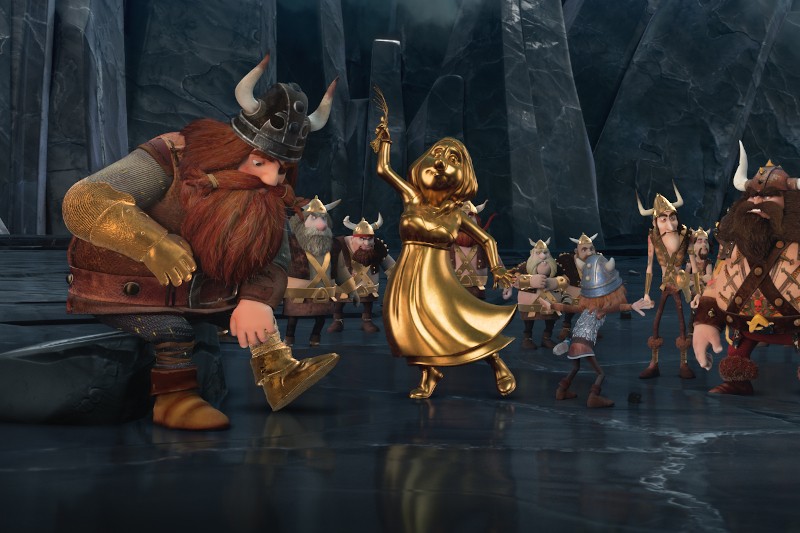 Grupa animowanych postaci wikingów stoi w ciemnej, lodowatej jaskini. Jeden duży wiking klęczy obok złotej statuy kobiety trzymającej patelnię, otoczony przez innych wikingów w hełmach i futrzanych ubraniach.