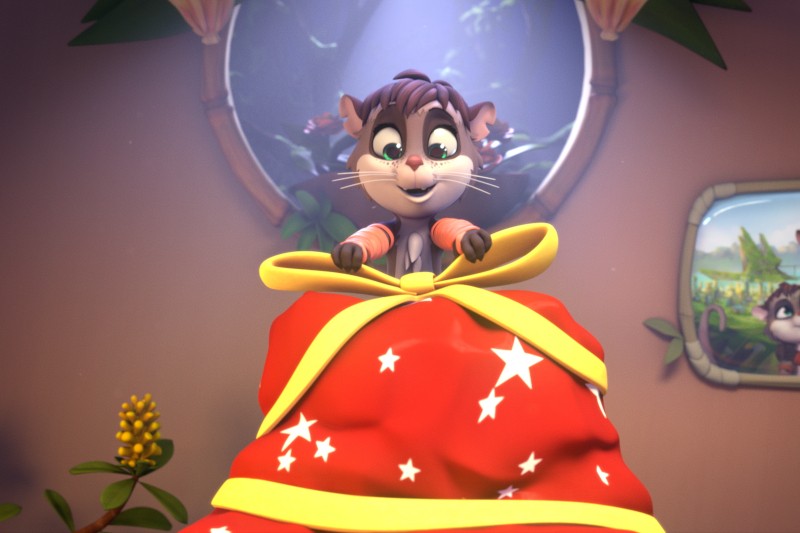 Animowana postać kota z ekscytacją patrzy na duży, czerwony, gwiaździsty prezent zapakowany w żółtą wstążkę. Scena jest jasna i radosna, z roślinami i oknem w tle.